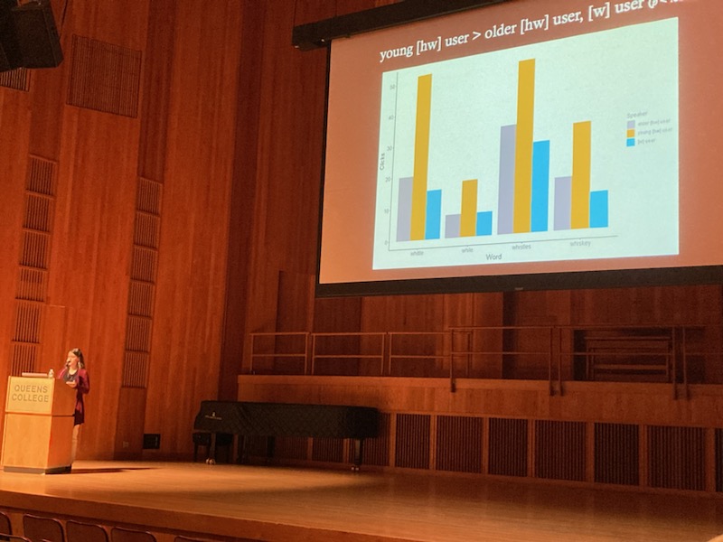 Keiko Bridwell on stage presenting her research. A bar graph is shown on a presentation slide.