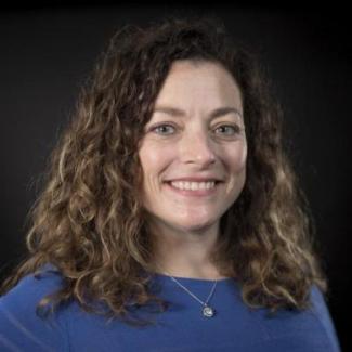 Portrait of Betsy Miller in blue shirt in front of black background