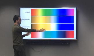 Joey Stanley standing in front of digital images of color examples