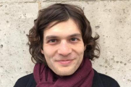 Dr. Jon Forrest standing in front of light brick wall with black coat and burgundy sweater