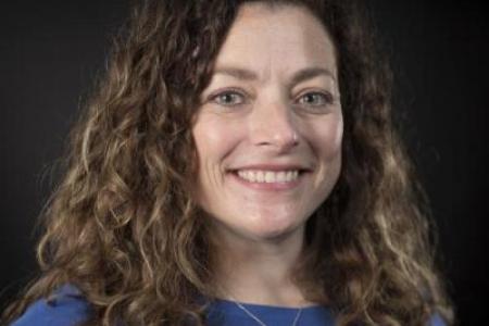 Portrait of Betsy Miller in blue shirt in front of black background